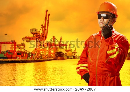Dock worker with radio communication for controlling work process commercial ship loading container in shipping port export nautical vessel transport and industry logistic in the harbor in sunrise