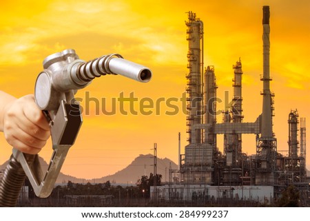 Hand holding a fuel nozzle pumping a benzine fuel and petrochemical oil refinery in beautiful sunrise