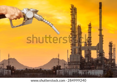 Hand holding a fuel nozzle pumping a fuel and petrochemical oil refinery in beautiful sunrise