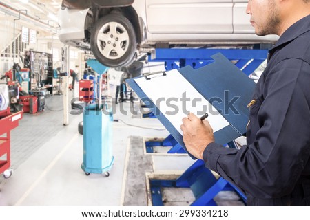 Mechanic recording a clipboard of service order for maintaining car on lift at the repair shop