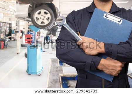 Mechanic holding a clipboard of service order and wrench for maintaining car on lift at the repair shop