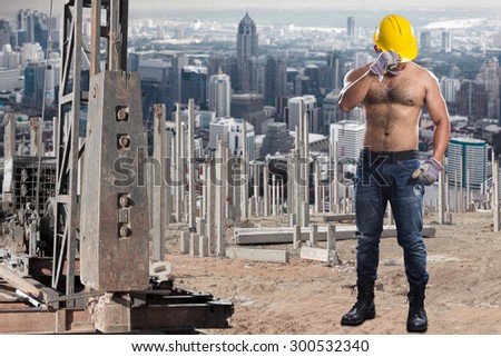 Brawny worker at pile driver works to set precast concrete piles in a construction site against city