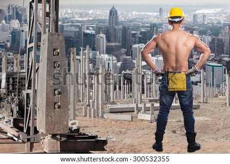 Brawny worker working at pile driver works to set precast concrete piles in a construction site against city metropolitan