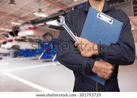 Car mechanic holding a clipboard of service order with wrench for maintaining car at the repair shop