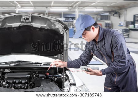 Auto mechanic uses a voltmeter to check the voltage level in a car battery at repair shop