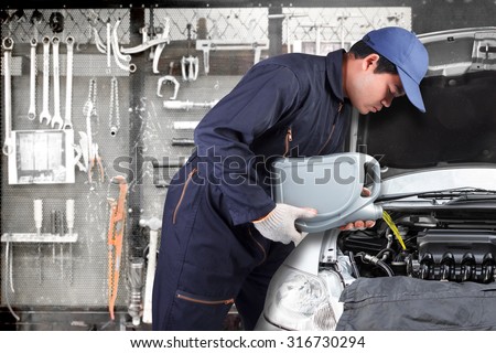 Car mechanic replacing and pouring oil into engine at maintenance repair service station with tools background