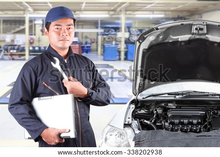 Auto mechanic holding computer and tool for service operation repaired at maintenance repair service station