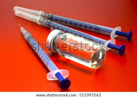 Vial with insulin hormone and  single use insulin syringes (pens) lying near the ampule. One syringe needle without cap. Set for diabetic problem. Red background.