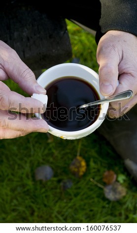 Man outdoors at coffee break holding a coffee cup and sugar piece in his hands, autumn weather