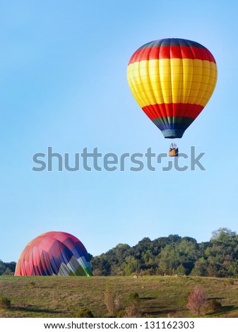 Hot air balloons landing in green hills with trees