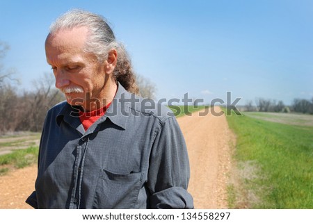 Sad looking man standing along a lonely dirt road