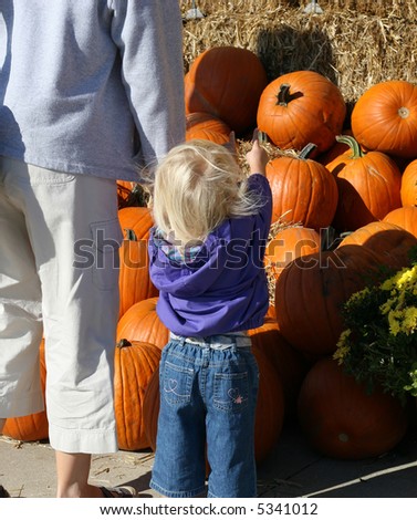 Girl picking out pumpkin with mom