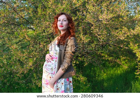 Beautiful pregnant woman near the cherry blossom branch. Red hair and lips. Beauty Model Girl . Perfect Creative Hair Style. Hairstyle. Future Mother
