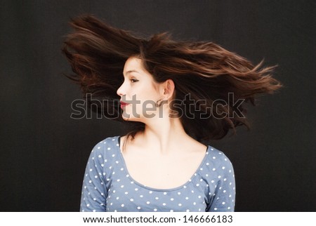 Portrait of a young  woman with polka dot dress and her hair in the wind over black background