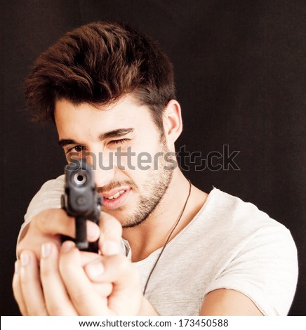 Handsome guy pointing a gun on black background