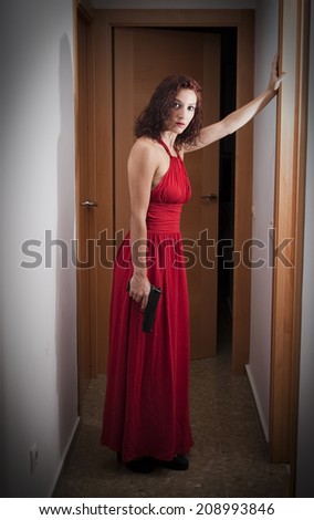 Portrait of Beautiful Young Woman  With a red dress and a gun in a hallway