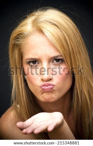Portrait of Beautiful Blonde Woman giving an air kiss Over Black Background