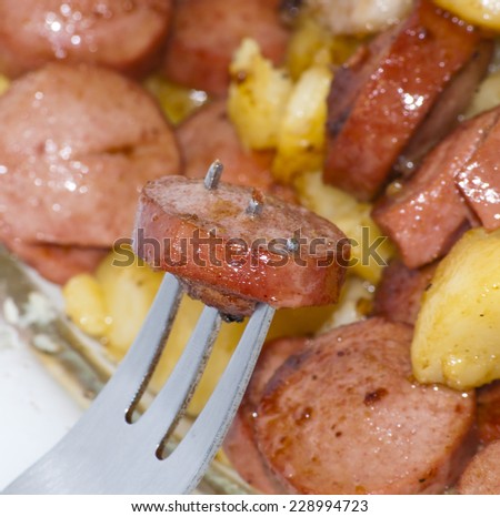 Plate of pieces of sausage, potatoes, garlic and meat with a piece of sausage on a fork punctured over white background