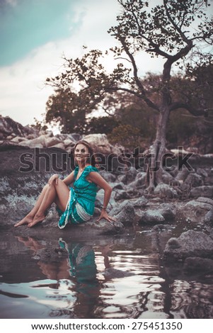 Young beautiful woman in long turquoise dress sitting on a stone by the sea. Retro colors