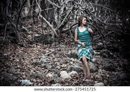 Portrait of a beautiful young woman in turquoise dress standing by trees In jungle forest. Retro colors on vintage card