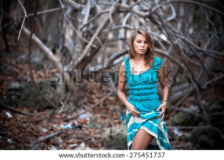 Portrait of a beautiful young woman in turquoise dress standing by trees In jungle forest