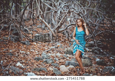 Portrait of a beautiful young woman in turquoise dress standing by trees In jungle forest. Retro colors on vintage card