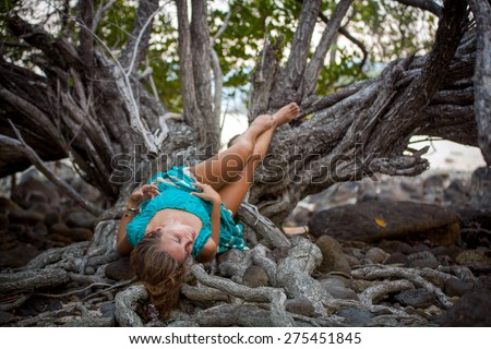 Beautiful young woman in a turquoise dress lying on roots of tree In the rainforest