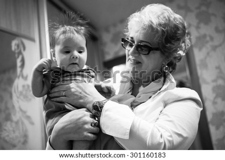 Baby boy in grandma\'s hands. Woman holding the baby and smiles. Black And white colors