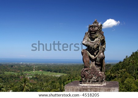 Balinese statue of a God chasing the evil spirits; terrace rice paddy and the ocean in the background