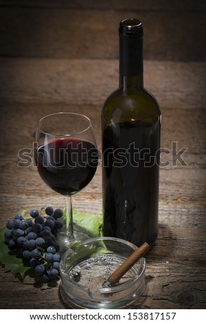 autumnal still life, grapes, wine glass, wine bottle and ashtray with cigar on old wooden