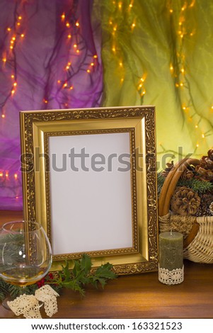golden frame with candle, brandy glass and cone basket on wooden in front of purple and green background