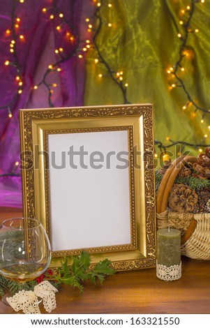golden frame with candle, brandy glass and cone basket on wooden in front of purple and green background