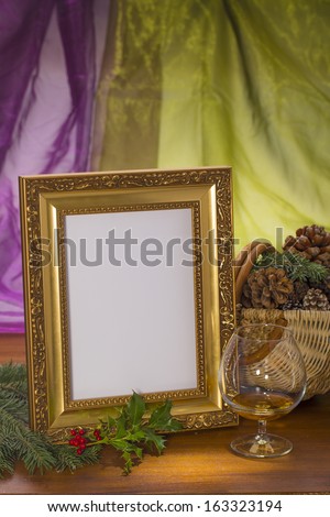golden frame with brandy glass and cone basket on wooden in front of purple and green background