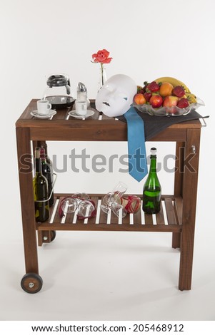 romantic tea-trolley with coffee, bottles, flower, mask and fruits