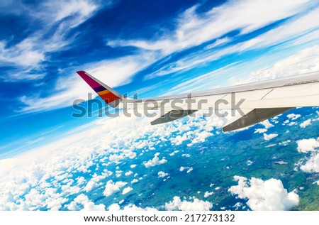 Wing of the plane on sky background - plane wing with cloud patterns - view from the window of a plane of the wing, the sky