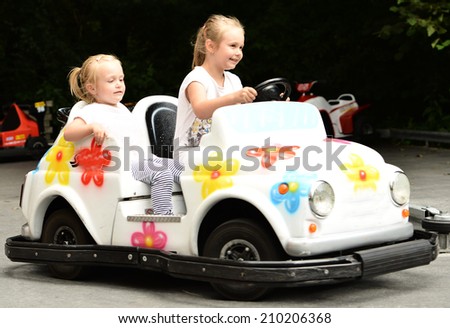 Two little girls riding toy car on streets of city.