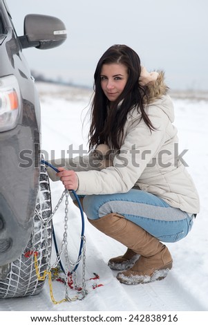 Woman putting winter tire chains on car wheel