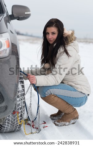 Woman putting winter tire chains on car wheel