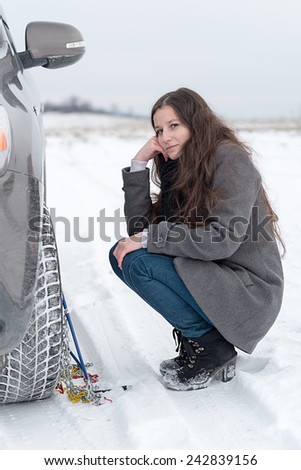 Woman putting winter tire chains on car wheel snow breakdown