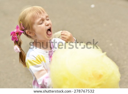 Adorable little girl eating candy-floss outdoors at summer