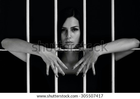Young woman looking from behind bars. trapped woman behind iron bars