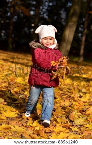 Small baby in autumn forest with yellow maple leaves