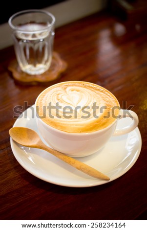 One white cup of Late and water stands on dark wooden table