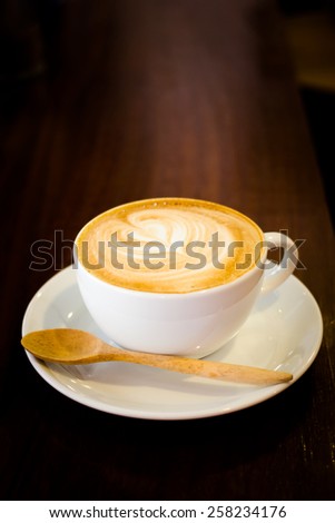 Close up white cup of Late art and spoon wood stands on dark wooden table