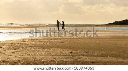Two people walking on a beach during sunset