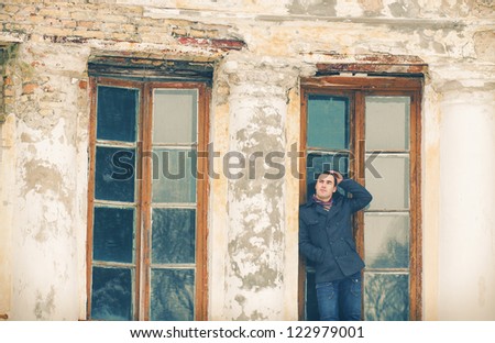 The man in warm jacket posing near an old house in winter