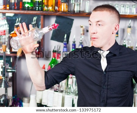 Young professional barman in action with shaker making cocktail drinks