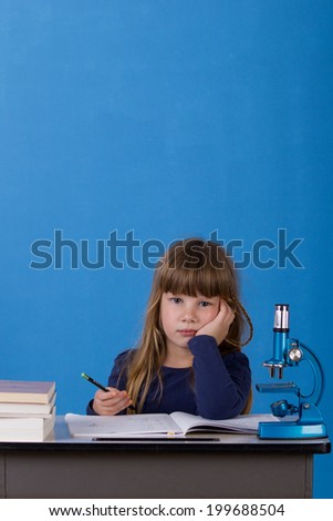 Little girl sitting at school table and writing