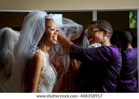 Mother of the bride adjusts her daughter\'??s veil on her wedding day.  Beautiful, African American women, smiling while getting the daughter ready for her wedding.