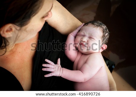 A woman holds her newborn son right after giving birth, they are still in the birthing pool after labor at home.